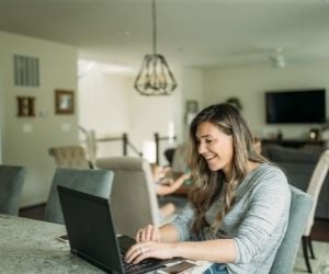 a white woman in a gray long sleeve shirt working from her laptop at home.
